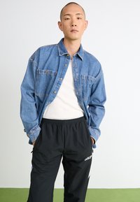 Denimskjorte, lys blå med to forlommer, båret over en hvid tanktop, parret med sorte træningsbukser med hvide striber og logo.