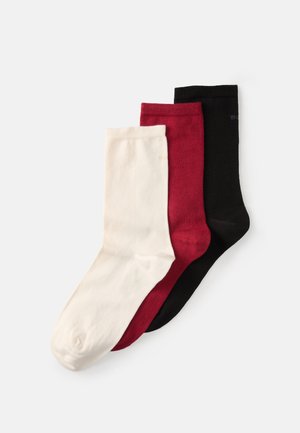 Tre par strumpor: en vit, en röd och en svart. Alla är släta, med design som går till mitten av vaden och subtila logotypdetaljer.