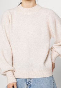 Pull en maille rose clair avec un col montant, des poignets et un ourlet côtelés. Il présente des manches ballon et une texture douce.