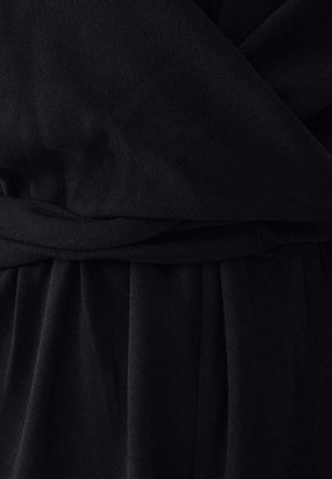 Detalle de un vestido negro con tejido suave y texturizado, con cintura fruncida y pliegues fluidos, destacando los elementos del material y del diseño.