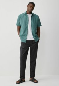 Chemise teal à manches courtes, t-shirt blanc en dessous, pantalon noir et sandales noires. Coupe décontractée avec des boutons sur la chemise. Texture plate.