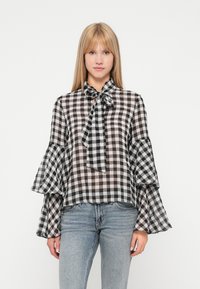 Melnā un baltā čekā stila blūze ar loku apkakli, caurspīdīgu audumu un izsāktām piedurknēm. Kombinēta ar gaiši ziliem džinsiem.