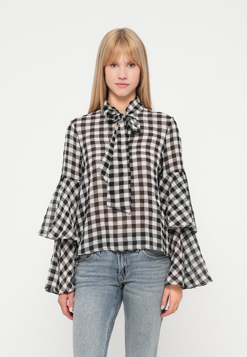 Melnā un baltā čekā stila blūze ar loku apkakli, caurspīdīgu audumu un izsāktām piedurknēm. Kombinēta ar gaiši ziliem džinsiem.