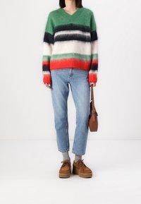 Multicolored striped sweater in green, white, red, and navy; round neckline and long sleeves; accompanied by light blue jeans and brown shoes.