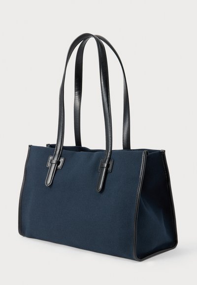 Τσάντα χειρός ορθογώνια σε ναυτικό μπλε με μαύρα δερμάτινα χερούλια και λεπτομέρειες, με δομημένο σχέδιο και ανοιχτό πάνω μέρος.