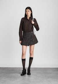 Ruda mygtukinė marškiniai, tamsių atspalvių plaid mini sijonas, juodos iki kelio kojinės ir juodi masyvūs batai. Laiko baltą frakcinį rankinuką.