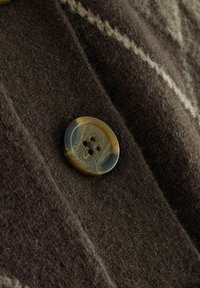 Brown woolen fabric with a soft texture, featuring a decorative striped pattern and a large, glossy faux horn button with four holes.