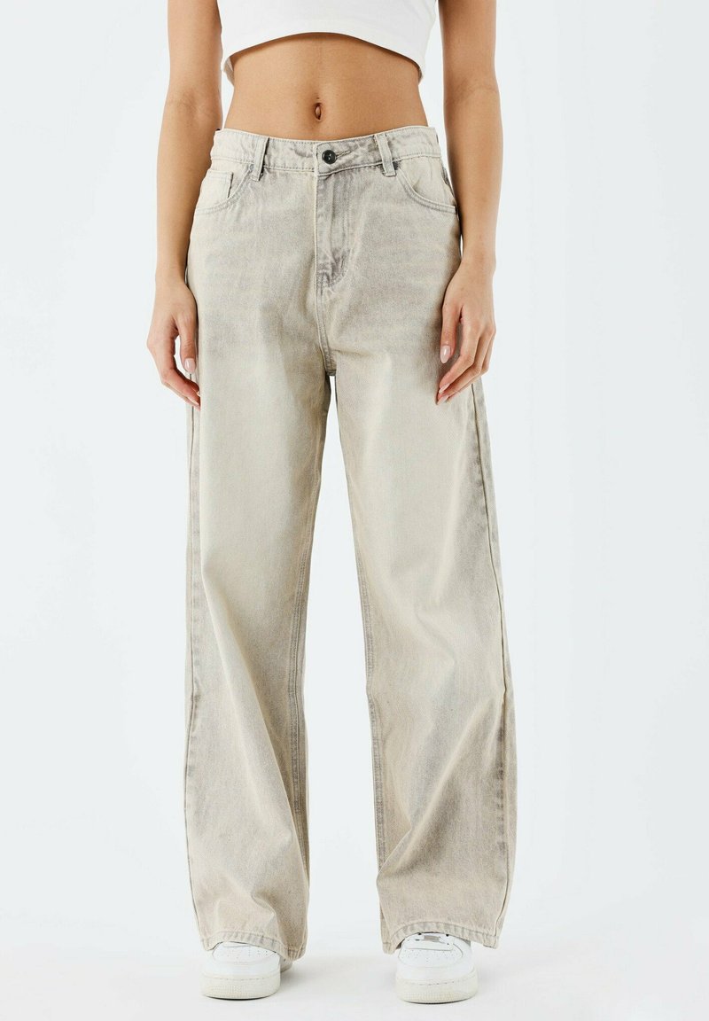 Jean large beige clair en denim, avec taille haute, fermeture à bouton sur le devant et deux poches latérales.