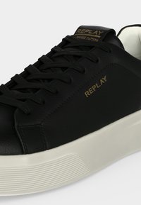 Baskets basses noires avec semelle épaisse blanche, lacets noirs et logo REPLAY doré sur le côté et la languette.