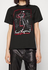 Camiseta de algodón negra con un diseño gráfico de bocetos de moda en blanco y rojo. Tiene un corte clásico y mangas cortas.