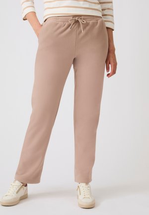 Persona che indossa pantaloni beige in pile con tasche frontali e vita con coulisse, abbinati a sneaker crema e un top a righe.