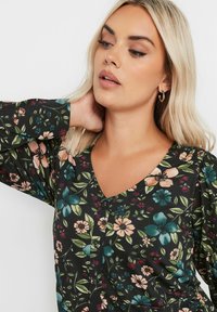 Kukkakuosiset paita mustalla taustalla, jossa on monivärisiä kukkia, V-pääntie ja napitusyksityiskohdat. Pitkät hihat joustavilla hiharesorreilla.