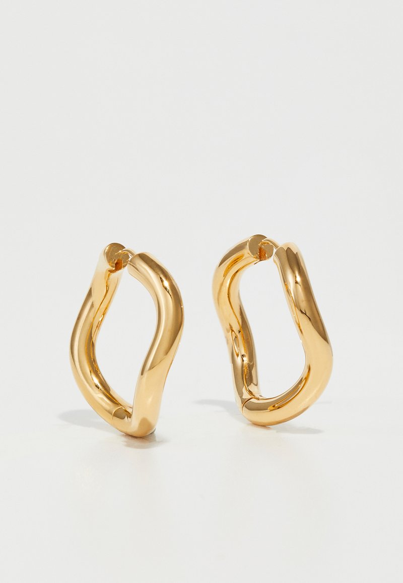 Zlaté kruhové náušnice s zakriveným, nepravidelným tvarom a hladkým, lesklým povrchom. Bez viditeľného hardvéru alebo akcentov.