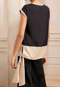 T-Shirt mit kurzen Ärmeln, schwarz auf der Vorderseite und beige auf der Rückseite, mit einem gebundenen Akzent an der Seite. Glatter Stoff mit lockerer Passform.