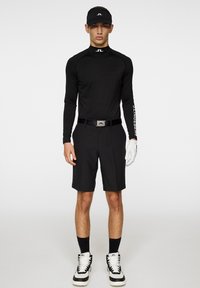 Czarna koszula z długim rękawem, czarne szorty, czapka z daszkiem w kolorze czarnym, biała rękawica. Obuwie ma czarno-biały design sięgający do kostki. Logo widoczne na koszuli i pasku.