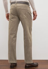 Pantaloni beige a gamba dritta realizzati in un tessuto morbido, con due tasche posteriori e una cintura, abbinati a scarpe scure.