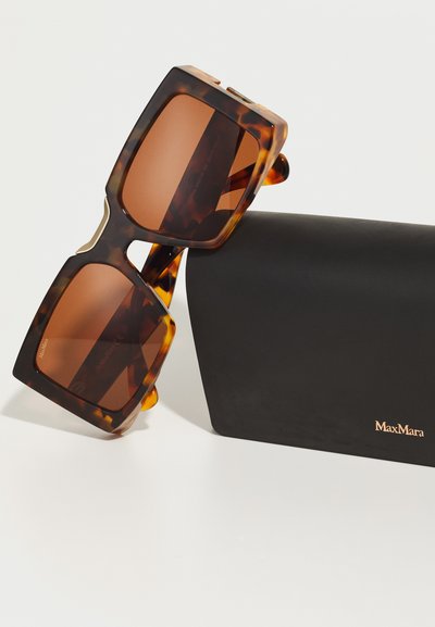 Kwadratowe okulary przeciwsłoneczne w musztardowym wzorze z brązowymi szkłami, z złotymi akcentami, umieszczone obok czarnego prostokątnego etui z logo "MaxMara".