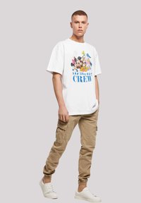 Hvit bomull t-skjorte med et fargerikt Disney-motiv som viser karakterer, kombinert med beige cargobukser og hvite joggesko.