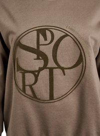 Hnědá mikina s velkým texturovaným logem "SPORT" v tmavě zelené barvě a kulatým designem. Nápis "Šampioni neustále hrají" vyšitý na rukávu.