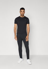 Zwarte t-shirt met korte mouwen en een subtiele logo op de borst, gecombineerd met strakke zwarte leggings en witte sneakers. Glad textuur van de stof.