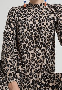 Šaty s leopardím potiskem, dlouhými rukávy, vysokým límcem a měkkou, splývavou látkou. Vyznačují se černými skvrnami na béžovém pozadí, které zvýrazňují strukturu.