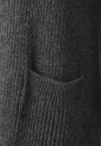 Suéter de punto gris oscuro con un patrón de relieve texturizado. Presenta un pequeño bolsillo en la parte delantera y una apariencia suave y acogedora.