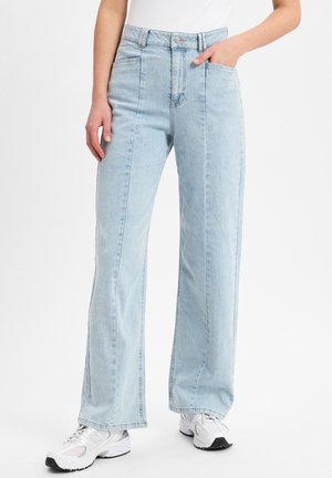 Lichtblauwe highwaisted wijde broek van denim, met voorzakken en een subtiele vervaagde textuur. Gepaard met witte sneakers.