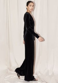 Jumpsuit in velluto nero con maniche lunghe, vita aderente e gamba ampia. Presenta una lucentezza sottile, una texture liscia e un design minimalista.