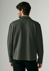 Chaqueta gris oscuro con un diseño estructurado, que incluye un cuello, mangas largas y costuras visibles. La tela tiene un acabado texturizado.