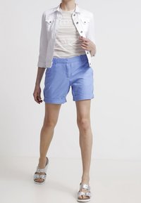 Shorts bleu clair avec revers, associés à une veste en jean blanche et un tee-shirt rayé de couleur claire. Sandales argentées complètent la tenue.
