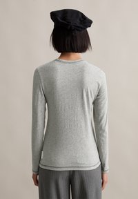 Graues langärmliges Shirt aus weichem, strukturiertem Stoff mit rundem Halsausschnitt und dezenten Nähdetails; getragen mit einer schwarzen Mütze.