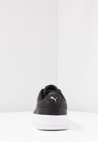 Sneaker in pelle nera con tomaia testurizzata, suola in gomma bianca e un piccolo logo bianco sul tallone. Design semplice con accenti minimi.