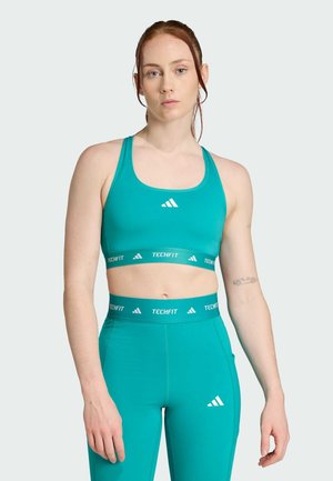 Tirkizni sportski top s visokim strukom i laminiranim tajicama s bijelim detaljima. Materijal je glatko i prilagođeno tijelu, s TECHFIT brendom i atletskim dizajnom.