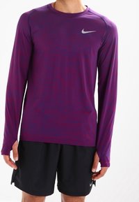 Długoslewy koszulka sportowa w kolorze fioletowym i magenta z teksturowanym wzorem, z srebrnym logo Nike na piersiach. Lekki materiał.