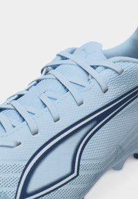 Svetlo modri nogometni čevelj Puma z teksturirano mrežico, svetlo modrimi vezalkami in temno modrim logotipom pasu na strani.