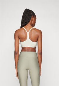 Sostenedor deportivo verde claro con espalda redondeada y tirantes finos, combinado con leggings de tiro alto con canalé en un tono verde claro a juego.
