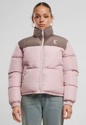 Doudoune avec un corps rose clair et une zone d'épaule marron, fermeture zippée et poignets élastiques, fabriquée dans un matériau lisse et rembourré.