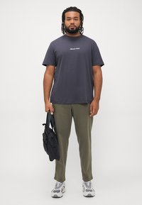 Mørk grå kortermet t-skjorte med hvit tekst, kombinert med olivengrønne bukser og svart veske, iført grå og hvite joggesko.