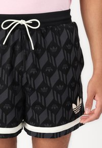 Black and grey athletic shorts featuring a repeated diamond pattern and Adidas logo. Elastic waistband with a white drawstring and trim.