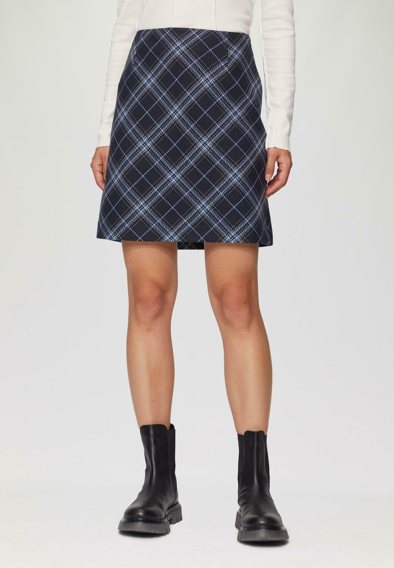 Granatowa spódnica mini w kratę z jasnoniebieskimi i zielonymi liniami, gładką teksturą i sylwetką w kształcie litery A, zestawiona z czarnymi botkami do kostki.
