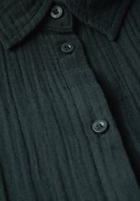 Camicia nera in tessuto texturizzato con colletto a punta. Presenta rigature orizzontali e cinque bottoni scuri lungo la placca.