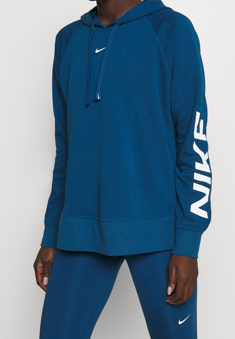Personne portant un sweat à capuche Nike bleu avec un logo blanc sur la poitrine et la manche, associé à des leggings bleus assortis avec un swoosh Nike blanc.