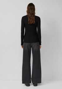 Zwarte langarmtop met een getailleerd lijfje en gestructureerde mouwen met kleine stippenpatronen, gecombineerd met wijde donkere grijze jeans.