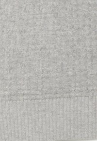 Hellgrauer gestrickter Stoff mit einem gerippten Rand und einem dezenten strukturierten Muster über dem Rippenmuster.