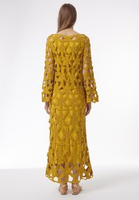 Robe au crochet jaune à manches longues, présentant un motif en dentelle floral et géométrique, avec un ourlet mi-mollet. Coupe élégante.