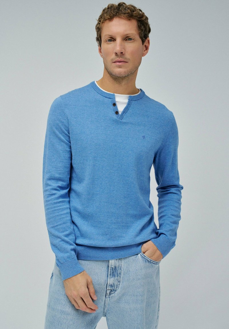 Maglione a maniche lunghe di colore blu chiaro in maglia con collo rotondo, caratterizzato da un abbottonatura a tre bottoni e polsini e orlo a costine. Abbinato a jeans di denim chiaro.