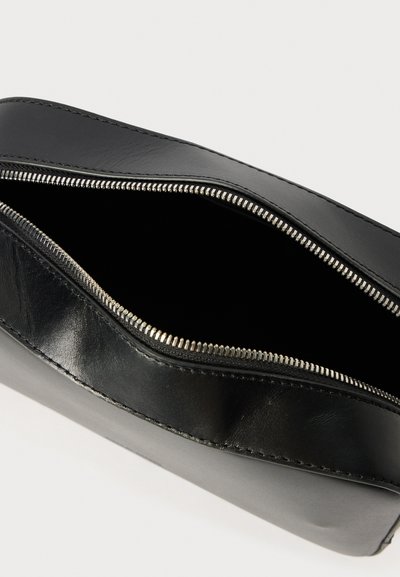 Černá kožená taštička s hladkým povrchem, se stříbrným zipem. Vnitřek je černý, s minimalistickým designem a bez dalších přihrádek.