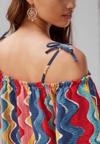 Haut coloré à épaules dénudées arborant un motif ondulé en rouge, bleu, jaune et rose, avec un tissu texturé et des bretelles en denim nouées en nœuds.