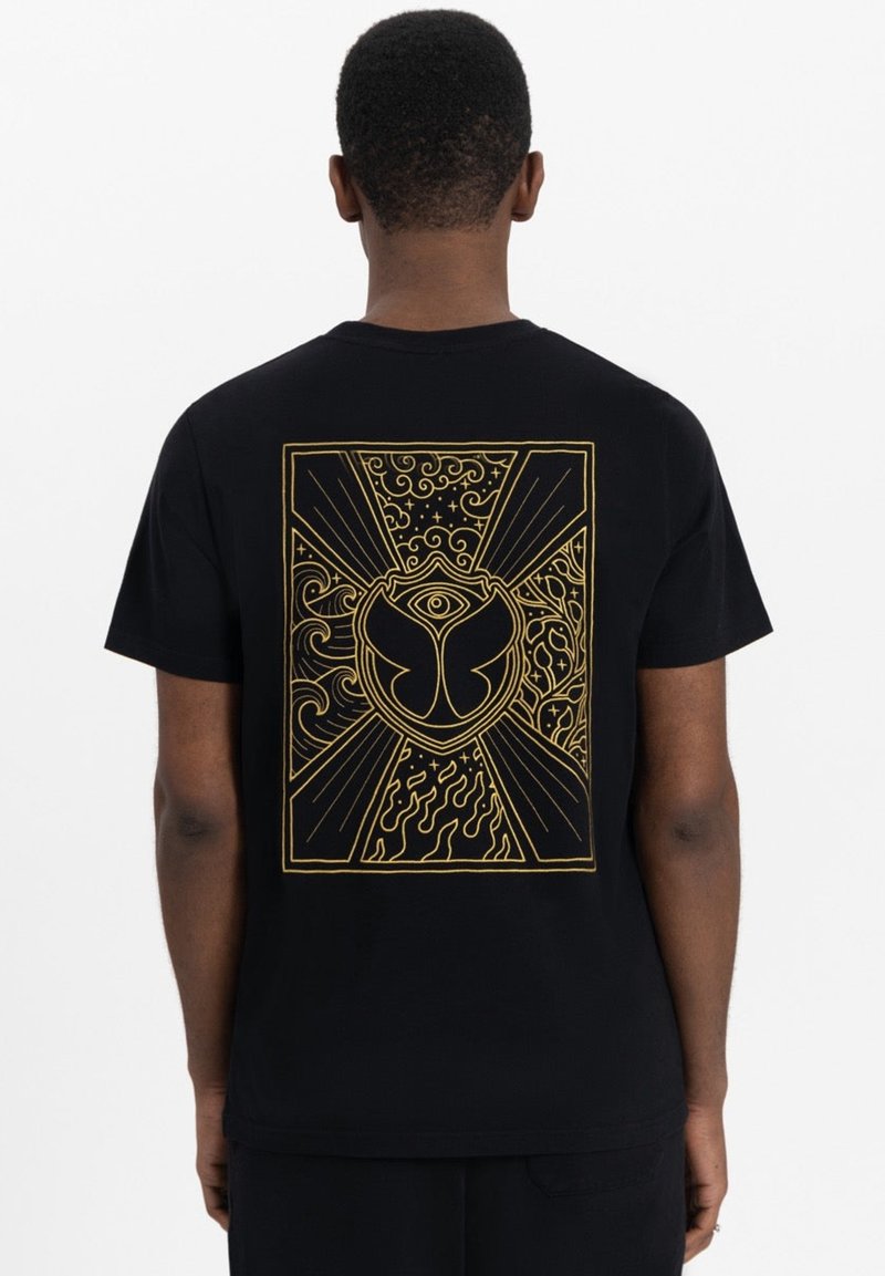 Zwarte t-shirt met een groot gouden grafisch ontwerp op de achterkant, met krullen, vlammen en een centraal embleem dat op een vlinder lijkt.