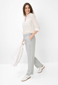 Linnen shirt in licht beige, met een knoopsluiting aan de voorkant en een pocket. Grijze linnen broek met een elastische taille. Witte sneakers.